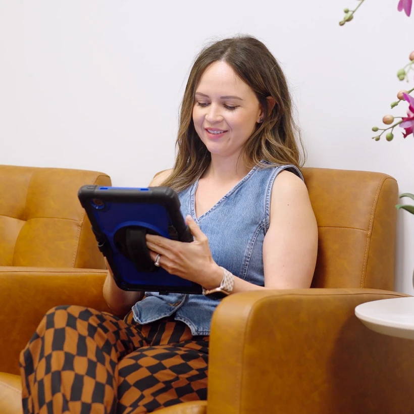 Woman sitting in a comfortable chair in the lobby using an iPad to check in at Conroe Dental Associates - Dentist in Conroe, TX